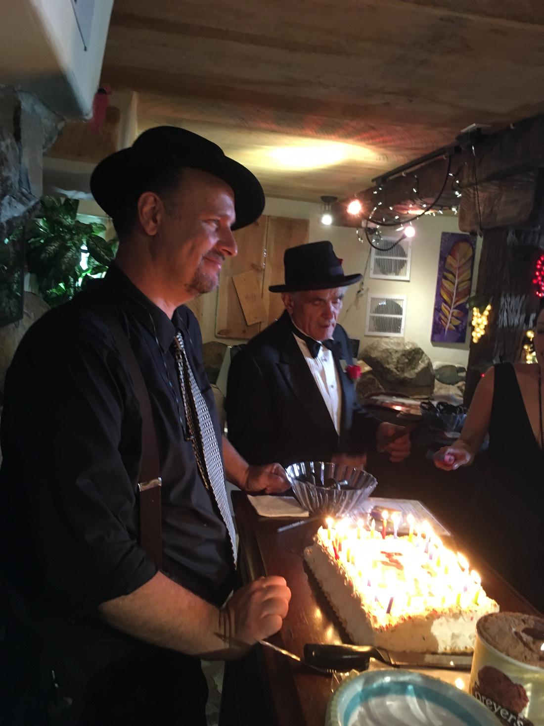 Members in hats serving cake at a cellar party