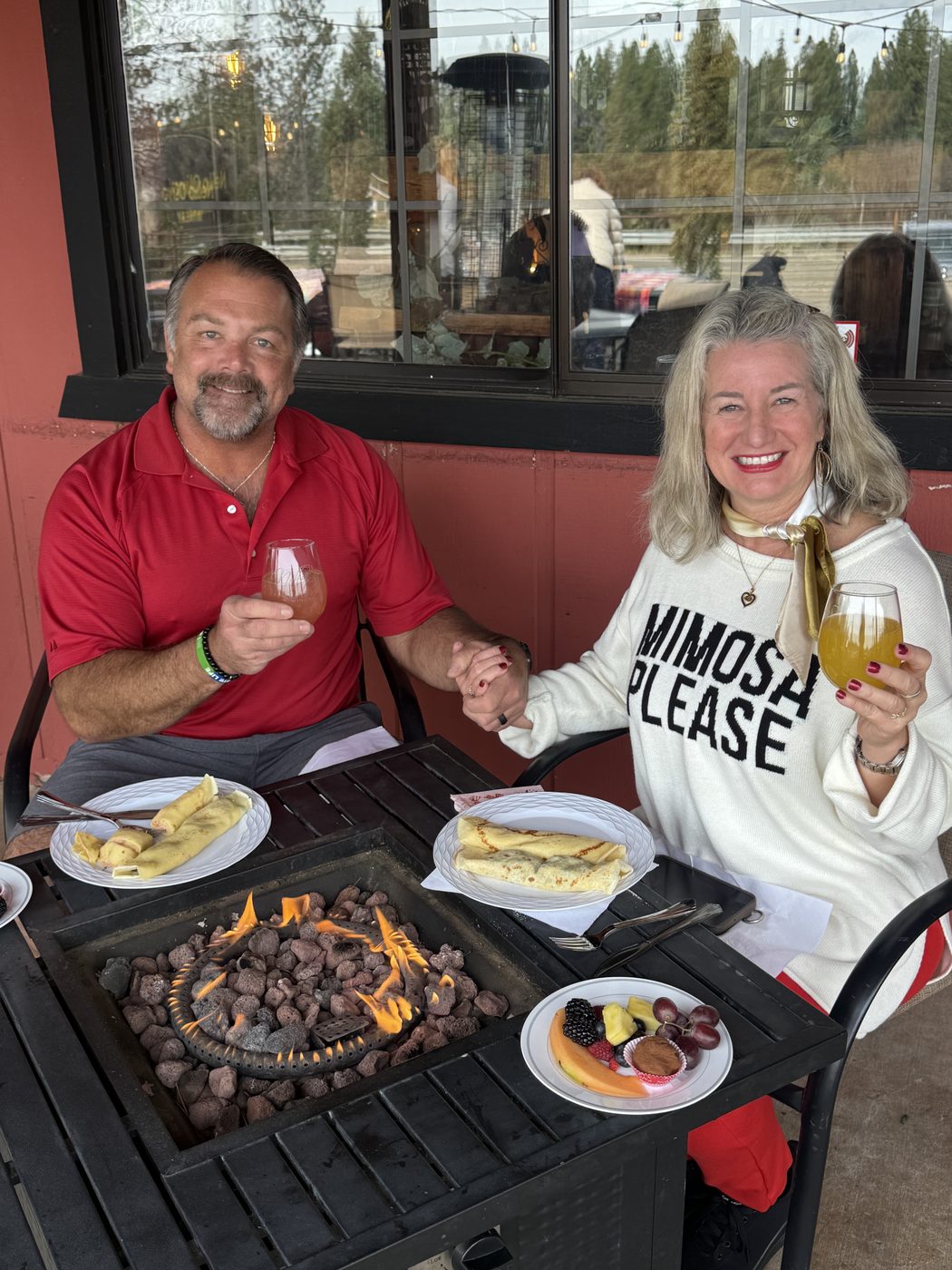 A couple over brunch at the patio fire table, mimosas in hand