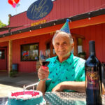 Man in birthday hat with wine glass sitting at table outside